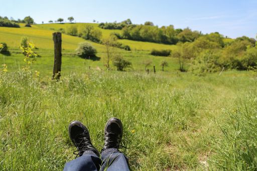 A selective focus shot of a greenfield with a person's feet on the grass