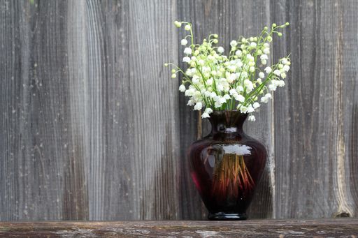 A closeup of lilies of the valley in a vase on a wooden surface