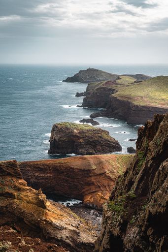 A vertical shot of cliffs near a sea with a cloudy sky background in Portugal