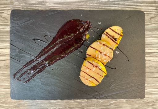 top view of a plate of fresh foie gras on a slate stone, with a red fruit jam on the side and coarse salt, on a wooden table
