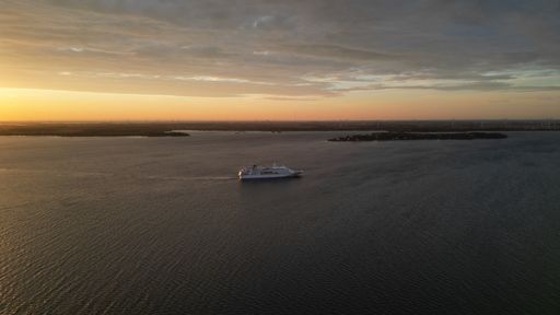 A scenic view of a cruise ship sailing by the coast with a beautiful sunset in the background