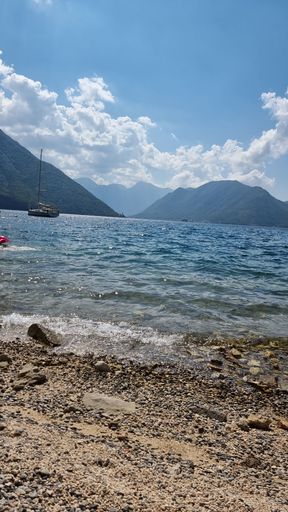 A vertical of a seacoast and a boat with the background of mountains
