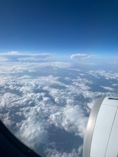 A vertical shot from airplane window of white fluffy clouds in the blue sky and the engine