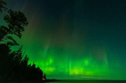 The aurora borealis over the lake surrounded by forest in Keweenaw Peninsula, Michigan