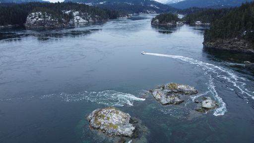 An aerial view of a boat speeding on Quadra island surrounded by trees and mountains