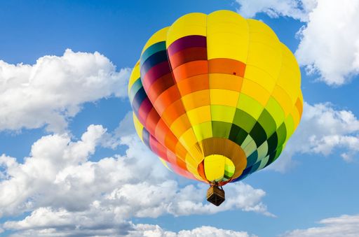 A low angle closeup shot of a colorful hot air balloon against a blue cloudy sky