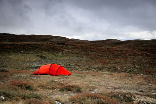 A beautiful shot of a red tent in a field under a cloudy sky