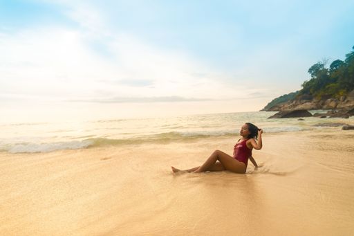 An attractive female wearing a red swimsuit sitting at the sandy beach during sunrise