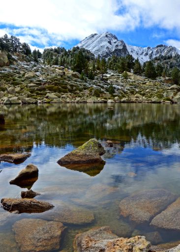 A vertical shot of a rocky snow-covered mountains with a reflection on a small lake