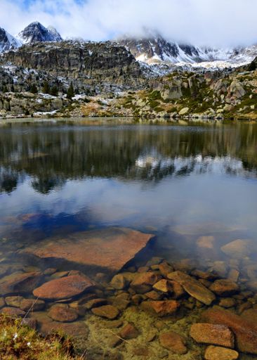 A vertical shot of a rocky snow-covered mountains with a reflection on a small lake