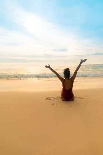A vertical shot of a female wearing a red swimsuit raising up her hands as a sign of freedom