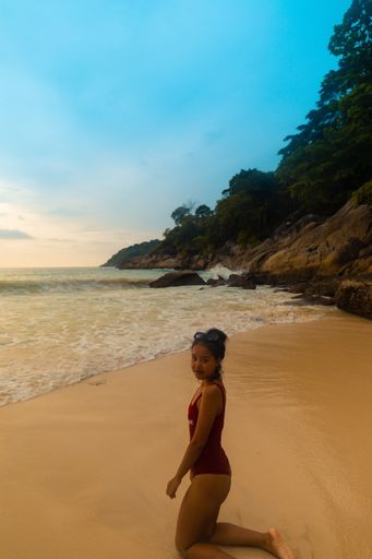A vertical shot of a female wearing a red swimsuit sitting at the sandy beach during sunrise