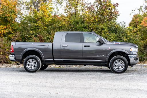 A side shot of gray 5th Gen Ram Laramie Mega Cab with Ram Box in the street in front of a garden