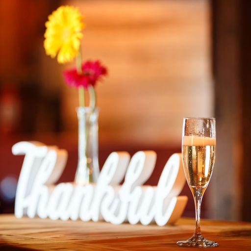 A closeup of a glass of champagne with a "Thankful" white figures and two flowers on the wooden table blurred background