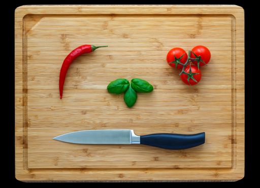 A high angle shot of a chopping board with a knife, chili tomatoes, tomatoes and mint leaves