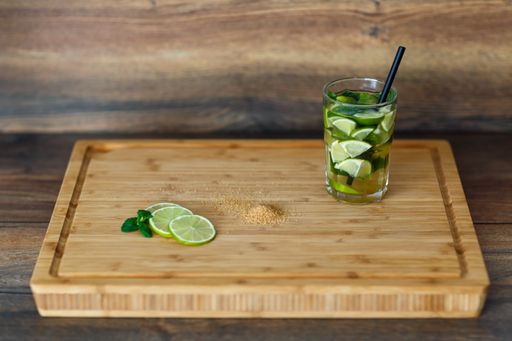 A wooden tray with a glass of Caipirinha drink made with lime and mint leaves