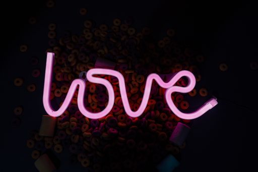 A top view of a neon ''Love'' sign surrounded by marshmallows and colorful cereals