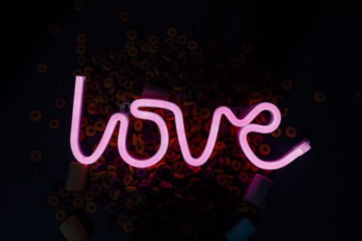 A closeup shot of a neon ''Love'' sign surrounded by marshmallows and colorful cereals