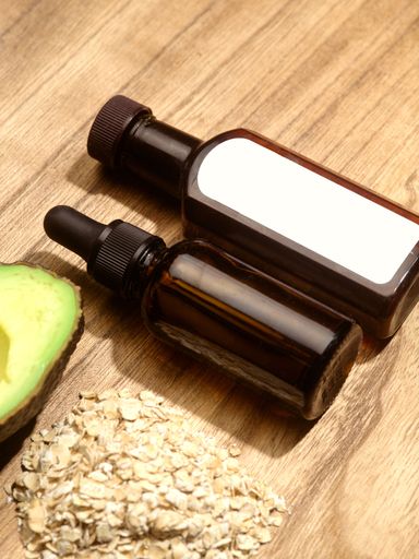 The two bottles of skincare serums with oat flakes and avocado nearby, a vertical closeup shot