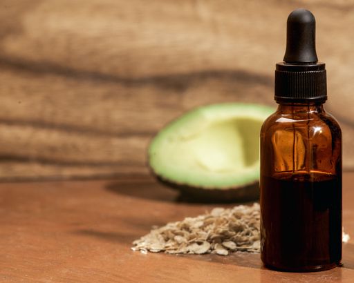 A closeup of a skincare serum bottle with oat flakes and avocado nearby
