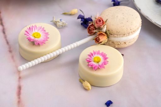 A top view of a wooden table with a macaroon on a stick and cakes decorated with dried flowers