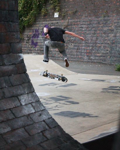A vertical back view of a male skateboarder making tricks in a park