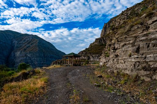 A view of a wooden hut with rocky mountains under the cloudy sky
