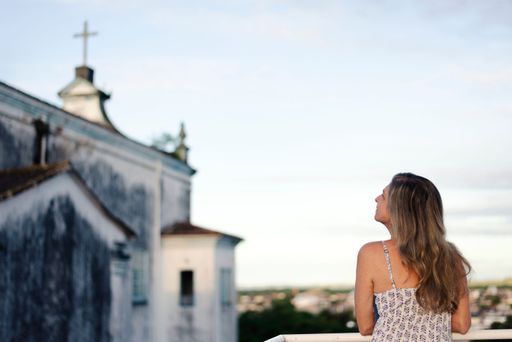 A woman on the porch with her back to the camera against the sky and church in the background.