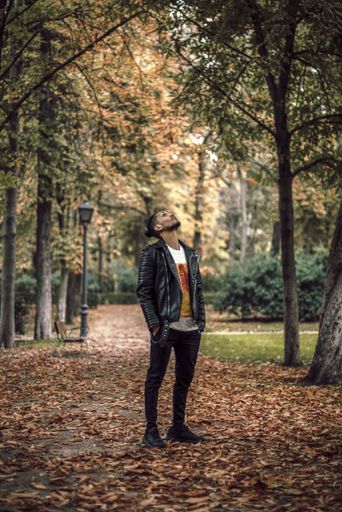 A young Hispanic male with a man bun standing in a park and looking up in autumn