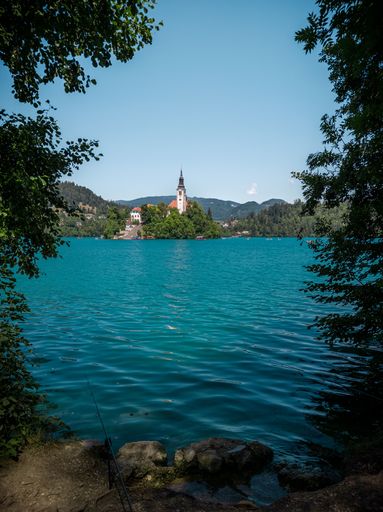 A vertical shot of the coast of a lake with a church in the other side on a sunny day