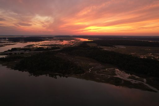 An aerial view of the Savannah river, surrounded by grass field, during an orange sunset