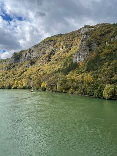 A forested mountain by the river against the background of the gloomy sky