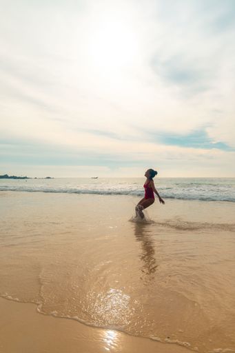 A vertical shot of a female wearing a red swimsuit getting ready to jump as a sign of freedom and happiness