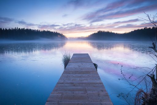 A scenic view of a wooden pier built on top of a lake with a beautiful landscape in the background