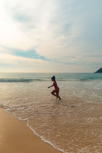 A vertical shot of a female wearing a red swimsuit running enjoying the fluffy bubbly ocean waves