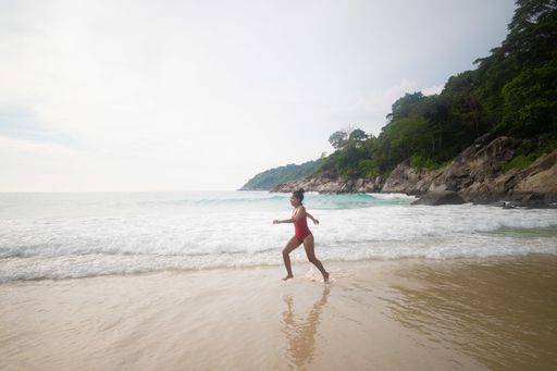 A female wearing a red swimsuit happily running at the beach enjoying the fluffy bubbly waves