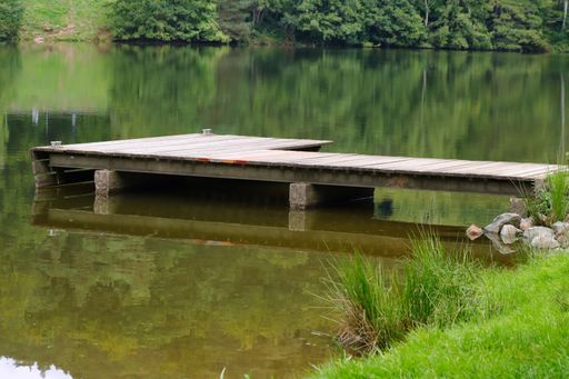 A wooden dock on a small lake with a forest in the background reflected in the waters during daytime