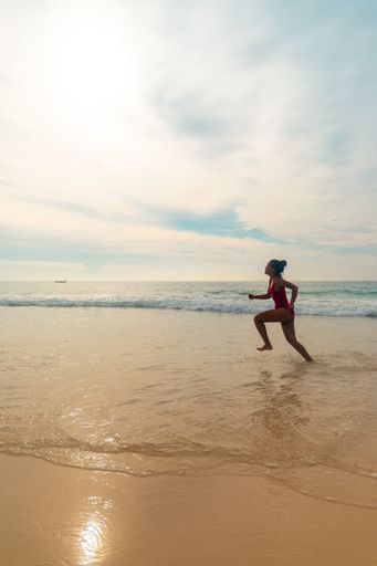 A vertical shot of a female wearing a red swimsuit running enjoying the fluffy bubbly ocean waves
