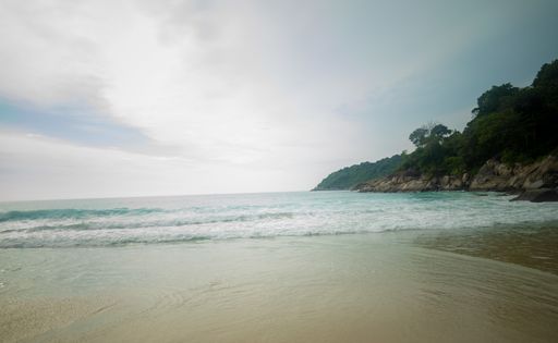 A breathtaking shot of the sun rising over the beach surrounded by a mountainous scenery