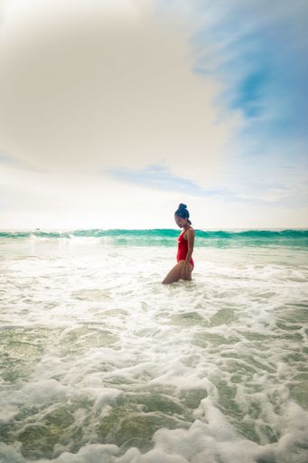 A vertical shot of a model wearing a red swimsuit enjoying the beautiful sunny weather in ocean waves