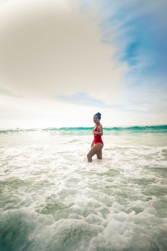 A vertical shot of a model wearing a red swimsuit enjoying the beautiful sunny weather in ocean waves