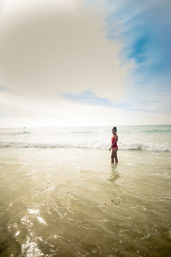 A vertical shot of a model wearing a red swimsuit enjoying the beautiful sunny weather at the beach