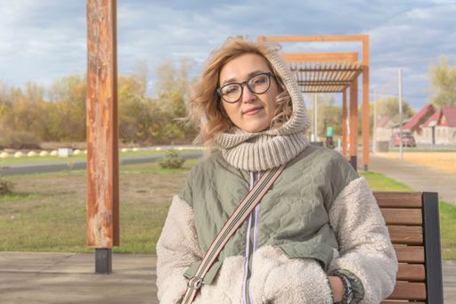 Young pretty blonde girl in warm autumn clothes sits in gazebo outdoors. Look in  camera. Hair blowing in the wind.