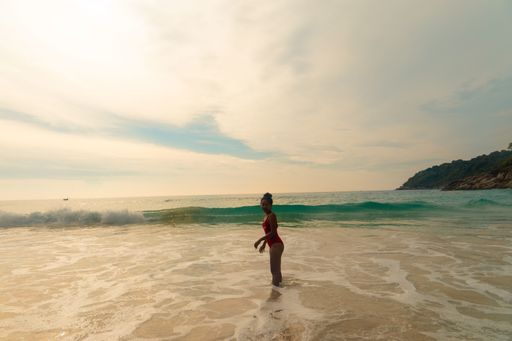 A beautiful shot of a female wearing a red swimsuit standing at the ocean shore during sunset