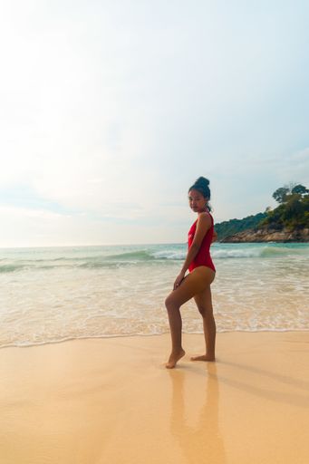 A vertical shot of a model wearing a red swimsuit enjoying the beautiful sunny weather at the beach