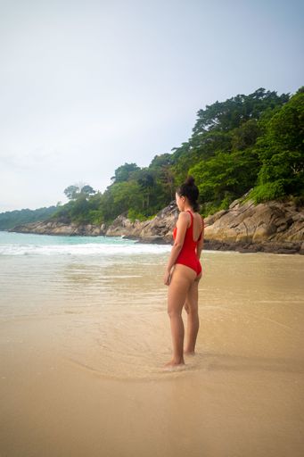 A vertical shot of a wearing a red swimsuit standing at the ocean shore enjoying the weather