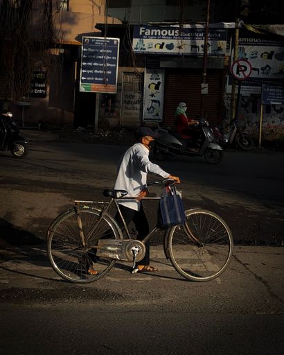 A vertical shot of a male walking while holding his bicycle in a poor district in Pune, India