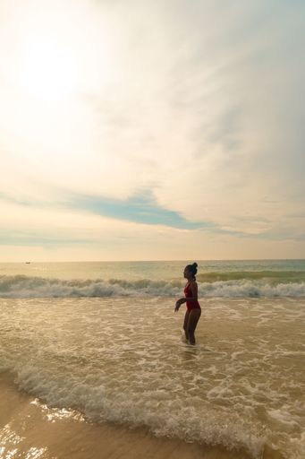 A vertical shot of a wearing a red swimsuit standing at the ocean shore enjoying the weather