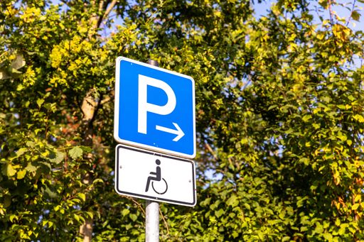 A low angle shot of a parking sign above the disability sign on a pipe surrounded by trees