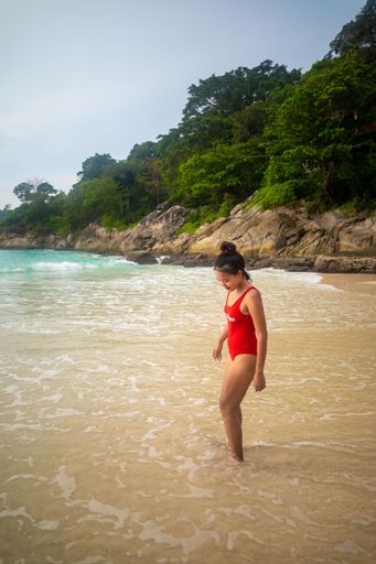 A vertical shot of a wearing a red swimsuit standing at the ocean shore enjoying the weather